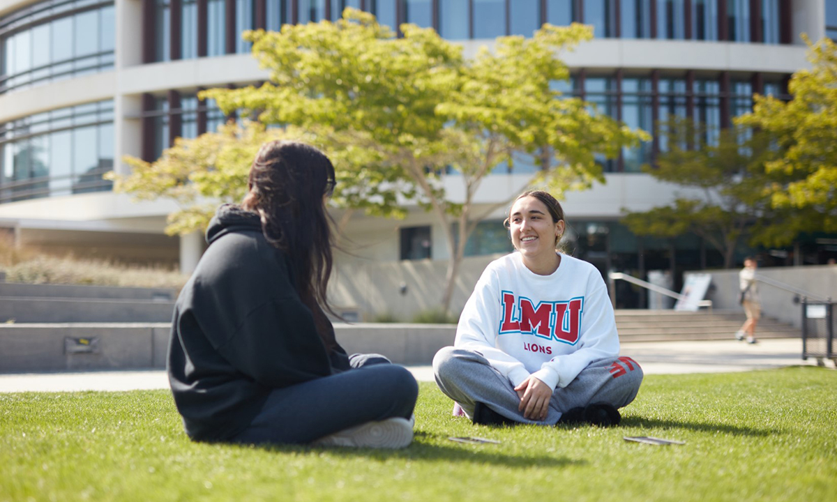 Two students sitting on the lawn outside the library